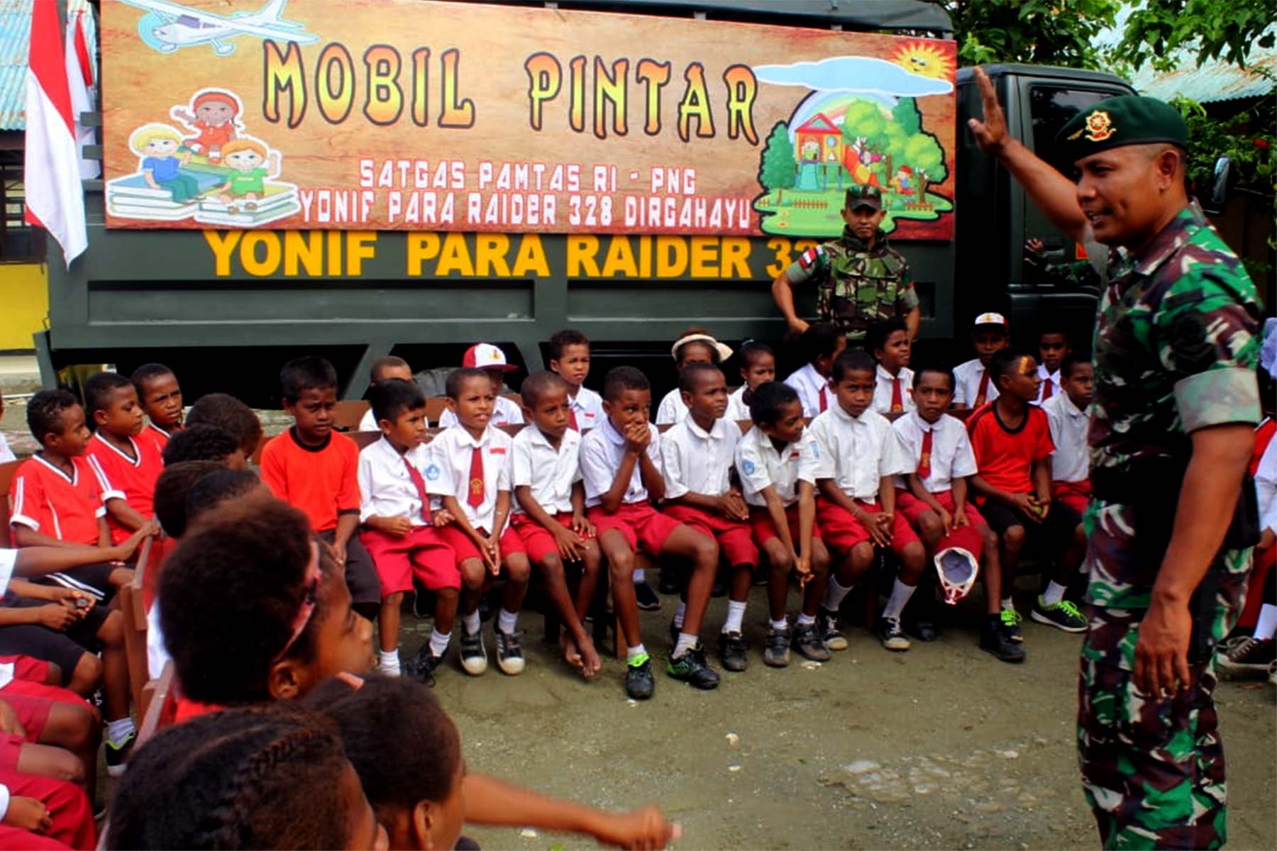 Salah satu anggota TNI yang bertugas di Pos Pamtas RI-PNG Yonif Para Raider 328/Dirhagayu sedang mengajar anak-anak di pedalaman Papua. Dibelakang mereka ada mobil pintar.