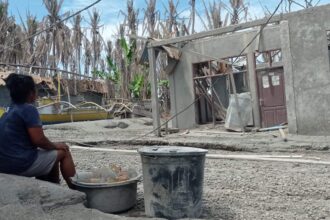 Bersama barang yang berhasil ditemukannya, Alfrida duduk menatap rumah yang iabangun bersama almarhum suaminya, (Foto: ZONAUTARA.com/Neno Karlina).