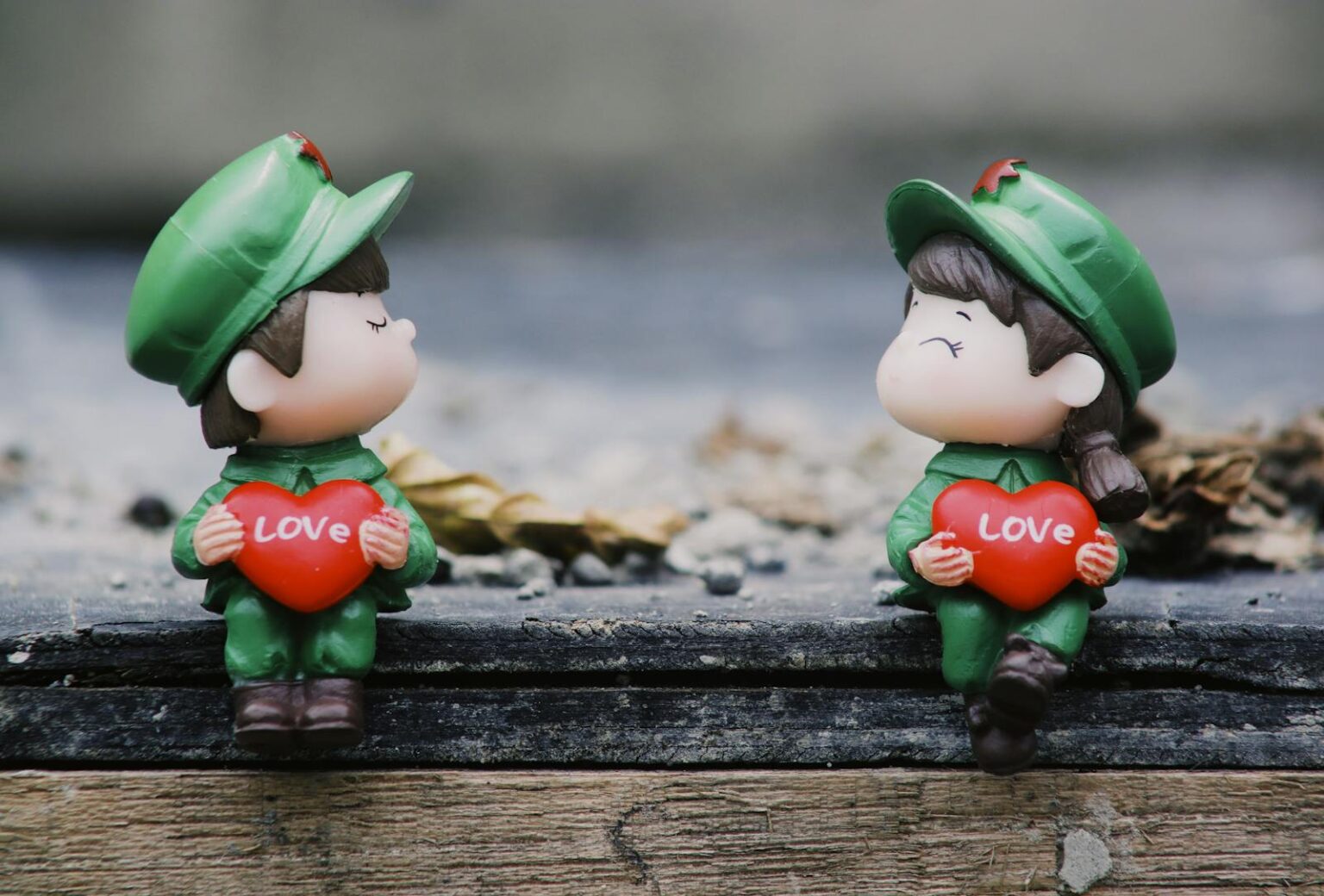 Adorable figurines in uniform holding red hearts with 'LOVE' inscribed, set on a wooden surface.