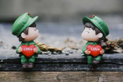 Adorable figurines in uniform holding red hearts with 'LOVE' inscribed, set on a wooden surface.