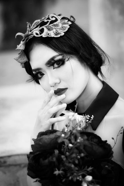 Black and white portrait of a woman with dramatic makeup holding flowers.